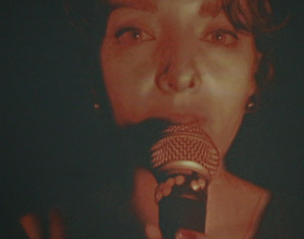 NINA singing into the mic, close-up, red stage light